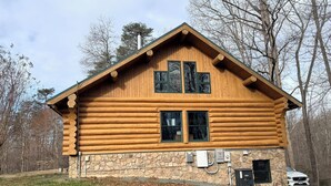 A log cabin with a stone foundation, two windows, and a chimney.
