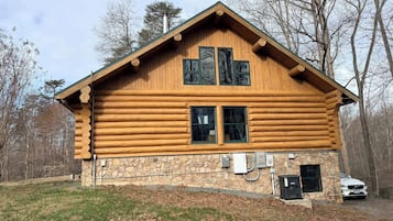Une cabane en rondins avec des fondations en pierre, deux fenêtres et une cheminée.