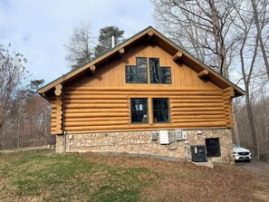 A log cabin with a stone foundation, two windows, and a chimney.