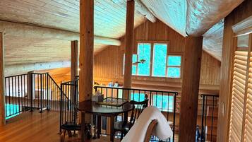 Un intérieur spacieux en bois, comprenant un coin repas, une grande fenêtre et un escalier.