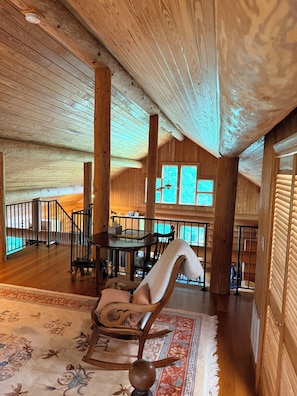 A spacious wooden interior with a dining area, a large window, and a staircase.