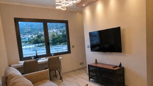 A modern living room with a sofa, dining table, TV, and a view of a mountainous landscape.