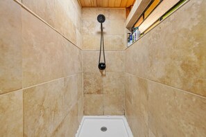 A shower with a handheld showerhead, tiled walls, and a wooden ceiling.