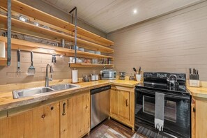Eine Küche mit Holzausstattung, einem Edelstahlspülbecken, einem Geschirrspüler, einer Mikrowelle, einem Herd und hängenden Küchenutensilien.