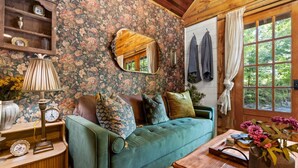 A cozy room with a green sofa, wooden shelves, a mirror, and a window with curtains. - Gilded Hideaway | Romantic Tiny Cabin in the Woods (Blue Ridge)