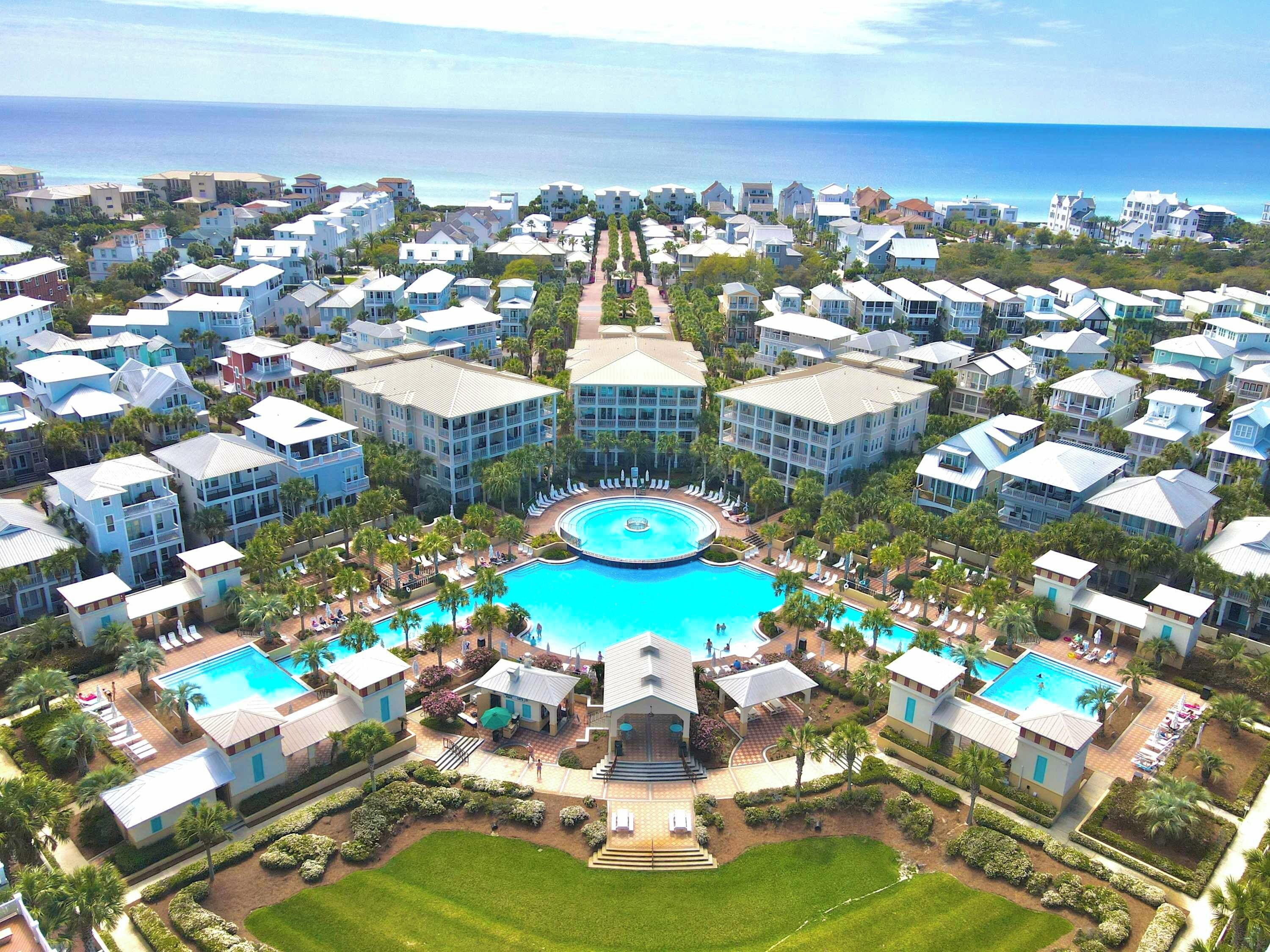 A resort with multiple buildings, a central pool, and a view of the ocean.