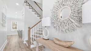 Un escalier avec des rampes en bois et un mur blanc orné d’un miroir décoratif et d’œuvres d’art mural.