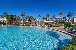 Une piscine d’un bleu éclatant, avec des chaises longues et des palmiers.
