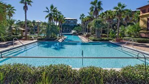 Une piscine offrant une vue dégagée, entourée de palmiers et d’immeubles.