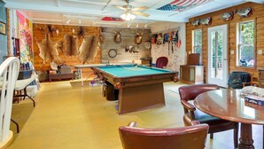 Una habitación con mesa de billar, sillones de cuero, dardo y monturas de animales en la pared.