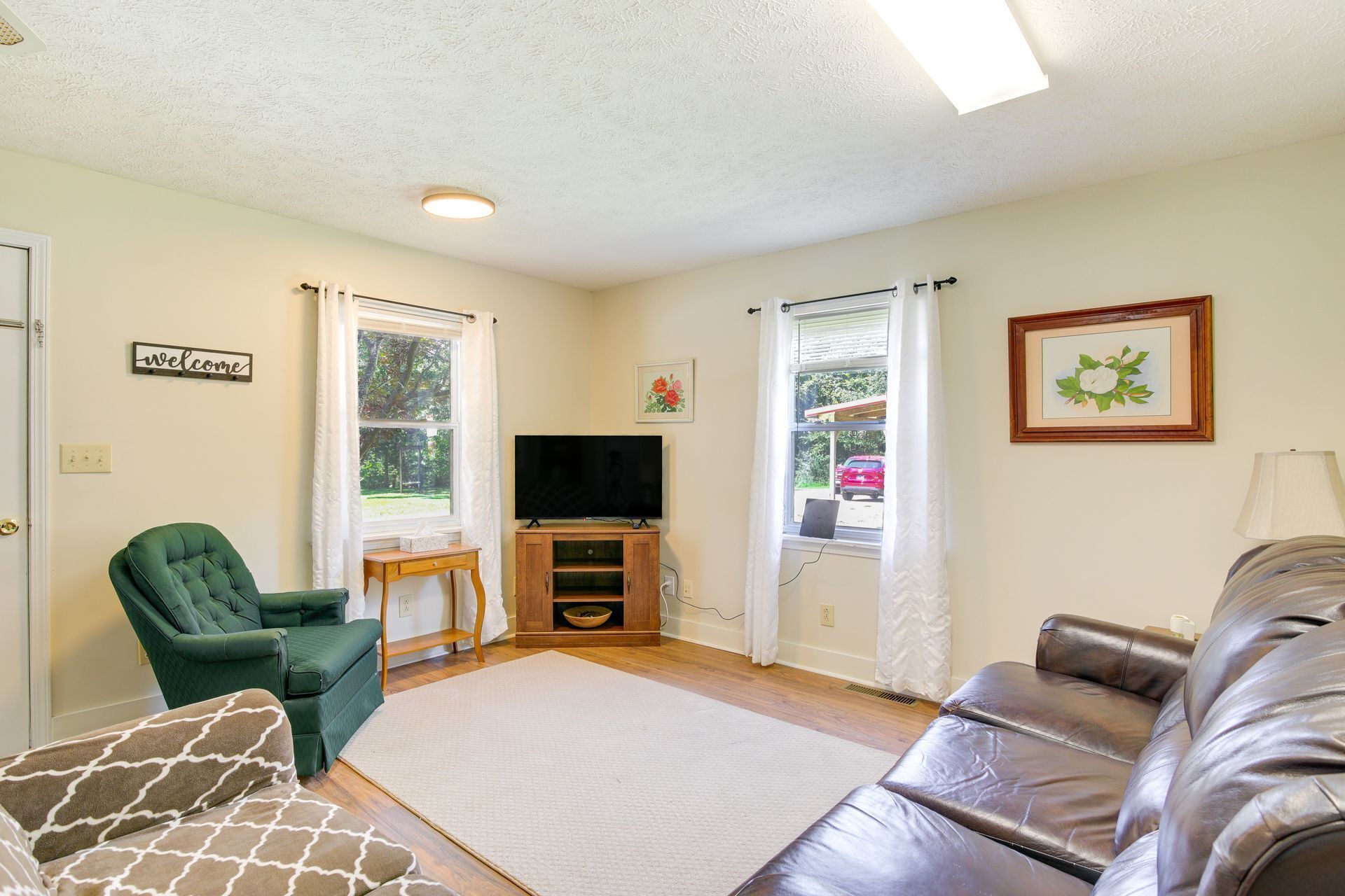 A living room with a green armchair, a brown sofa, a flat-screen TV, and a small wooden table.