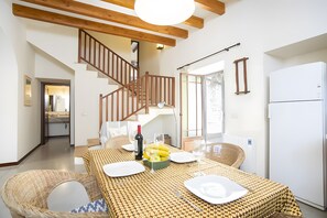 A dining area with a table set for two, a bottle of wine, and a fruit bowl. A staircase is visible in the background. - Ca sa padrina. tradition and charm in mallorca (Artà)