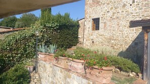A stone building with a window and a garden with potted plants and flowers.