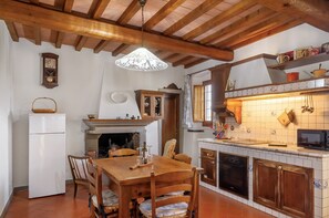 A kitchen with wooden beams, a dining table, chairs, a refrigerator, a microwave, and a tiled backsplash.