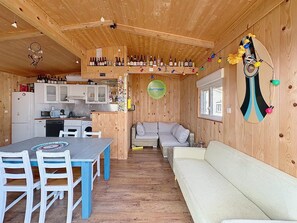 Ein Interieur einer Holzhütte mit Esstisch, Stühlen, einer Couch, einer Küchenzeile und einer Wand, die mit Flaschen und Lichterketten dekoriert ist.