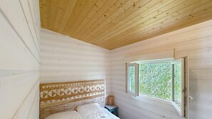 A bedroom with a wooden headboard, a bed with white bedding, a small table, and a window with a view of greenery. - 8-BERTH CHALET WITH LARGE TERRACE (Gruissan)