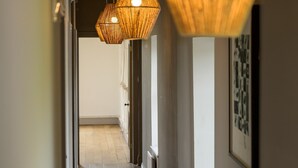 Un couloir se terminant par une porte en bois, un tableau encadré au mur et un luminaire suspendu au plafond.