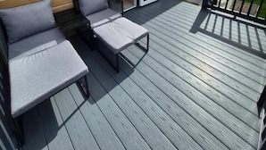 A wooden deck with two grey cushioned chairs and a small table. - Cosy Lodge in North Devon with Private Parking (Ilfracombe)