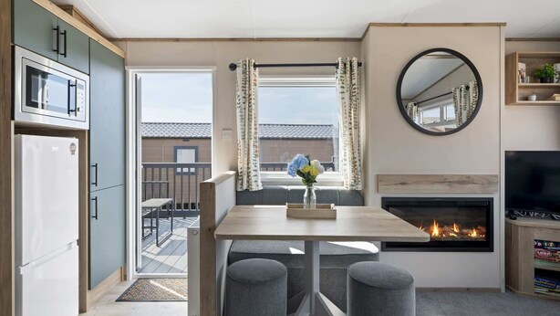 A compact kitchen with a microwave, refrigerator, and dining area with a table and two chairs. - Cosy Lodge in North Devon with Private Parking (Ilfracombe)