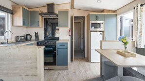 A compact kitchen with a stove, microwave, and sink. - Cosy Lodge in North Devon with Private Parking (Ilfracombe)