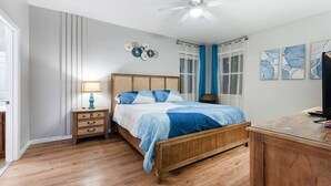 Una camera da letto con un letto in legno, un comodino con una lampada, una ventola a soffitto e opere d'arte alle pareti.