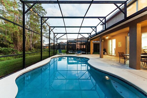 Una piscina con cerramiento de vidrio, rodeada por un patio amoblado con mobiliario exterior.
