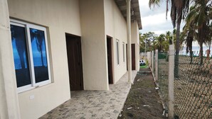 A building with a stone-tiled walkway, a chain-link fence, and a view of palm trees.