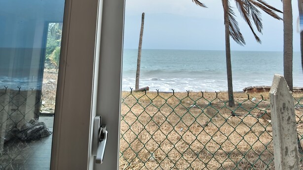 A view through a glass door to a beach with palm trees and a fence.