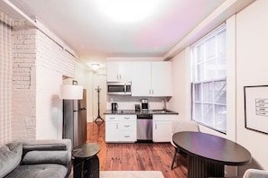 A compact kitchen with white cabinets, a refrigerator, a coffee maker, and a dishwasher. - Cedar & Brick on the Hill (Boston)