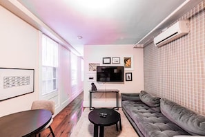 A living room with a sofa, a coffee table, a TV, and framed pictures on the wall. - Cedar & Brick on the Hill (Boston)