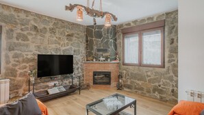 A living room with a stone wall, a fireplace, a television, and a glass coffee table.