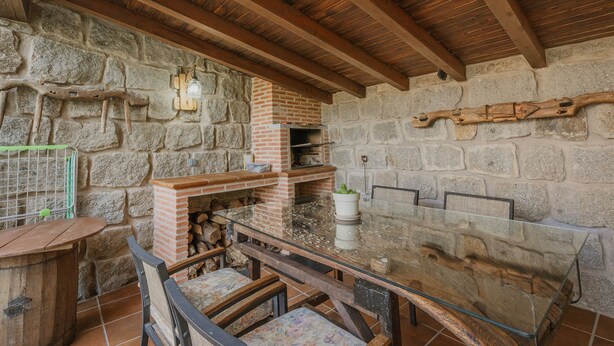 A rustic stone wall with a brick fireplace, wooden beams, and a glass table with chairs.