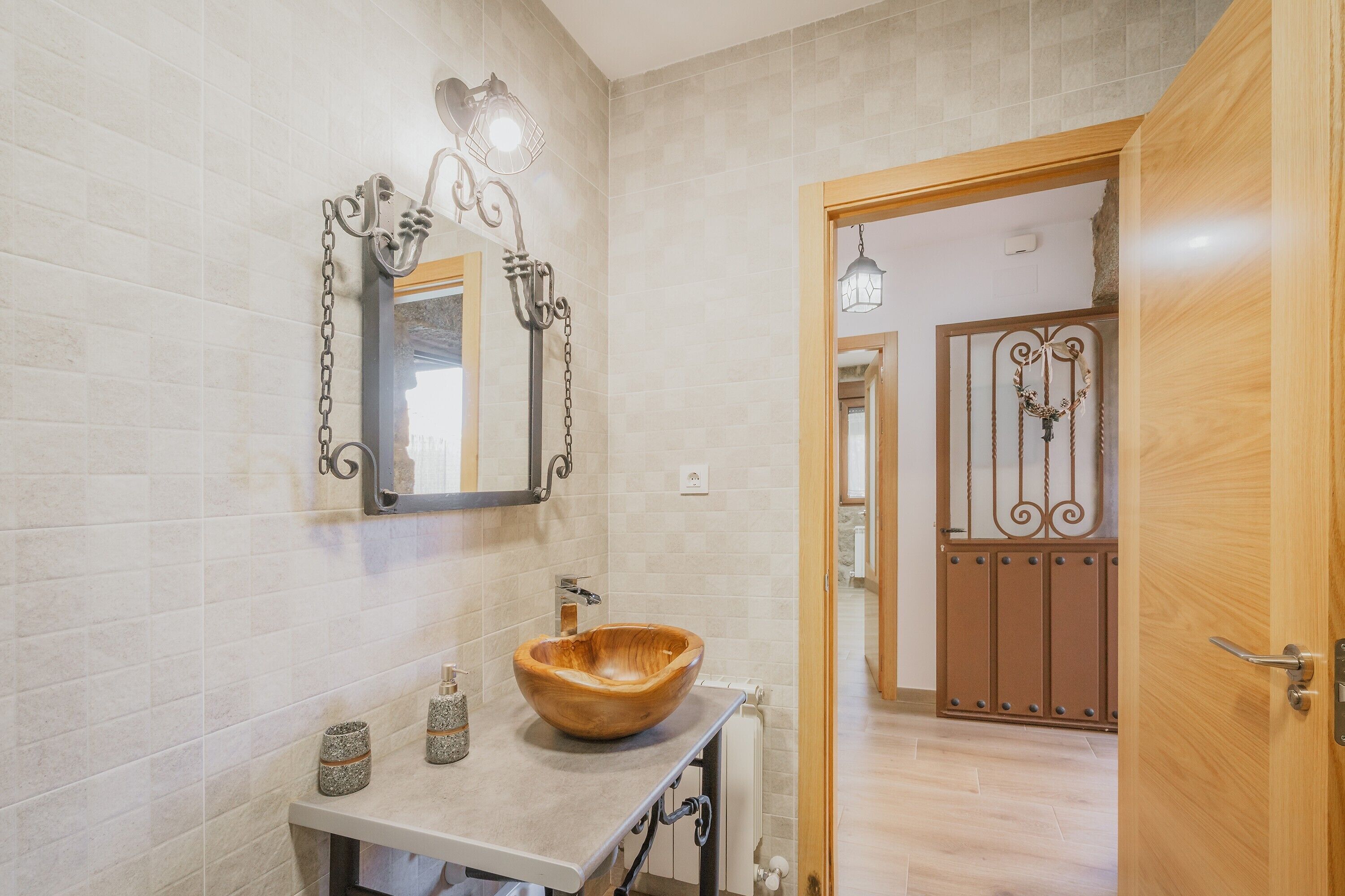 A bathroom with a wooden bowl sink, a mirror with a decorative light fixture, and a door leading to another room.