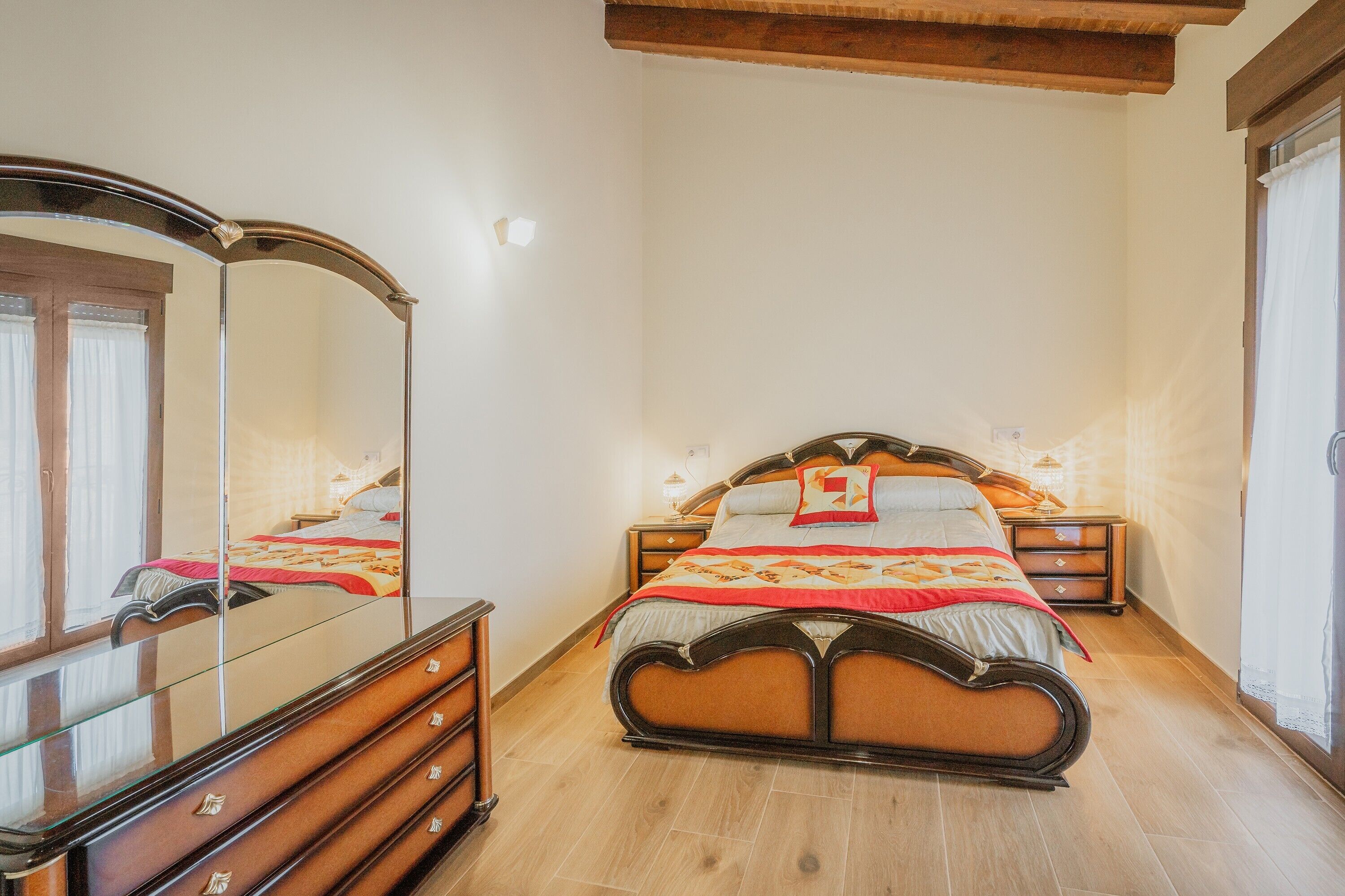 A bedroom with a bed, dresser, mirror, bedside tables, and a window.