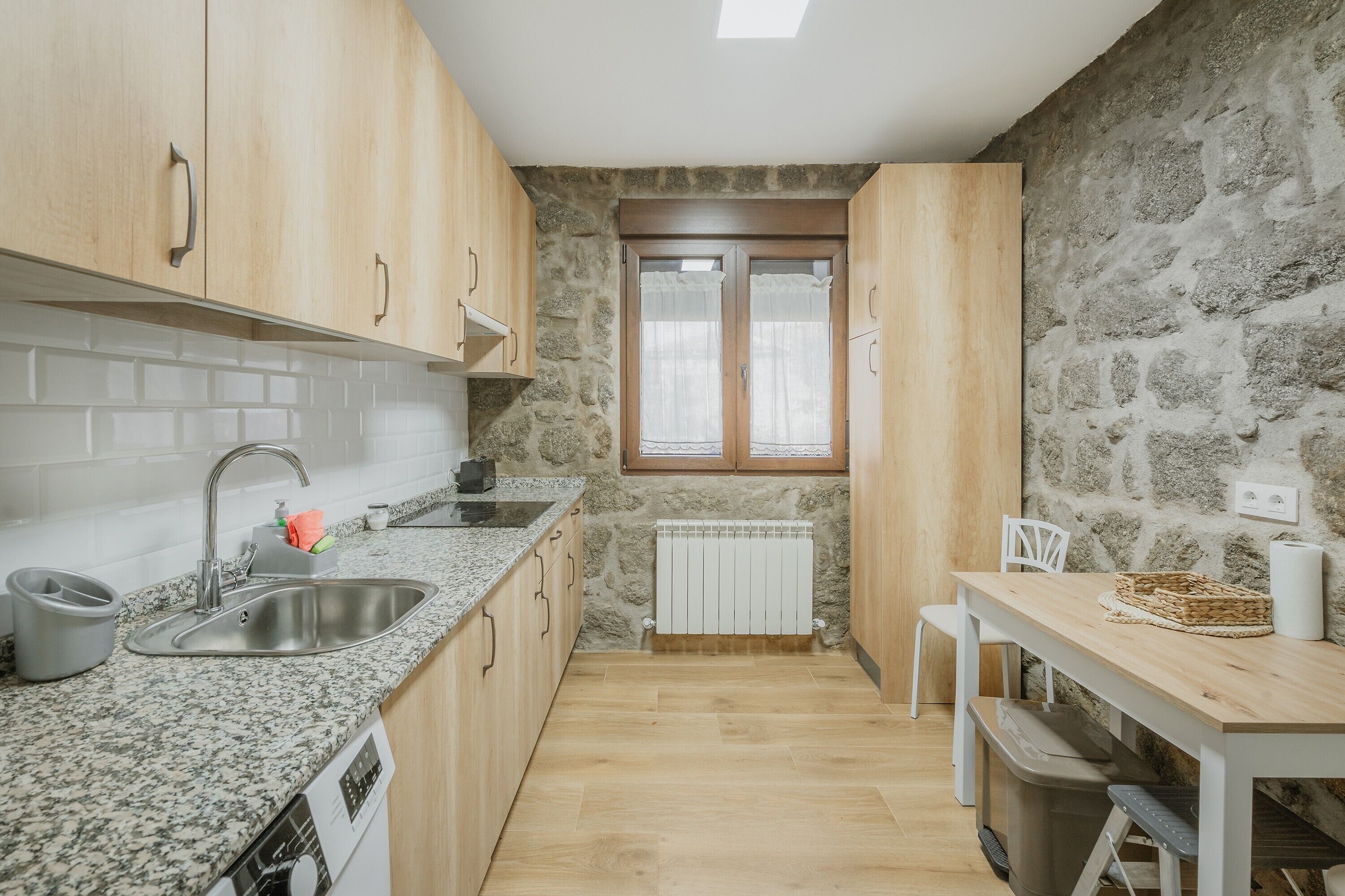 A kitchen with granite countertops, wooden cabinets, a stone wall, a window, and a radiator.
