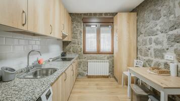 A kitchen with granite countertops, wooden cabinets, a stone wall, a window, and a radiator.