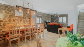 A dining area with a stone wall, wooden chairs, a glass table, and a green tablecloth.