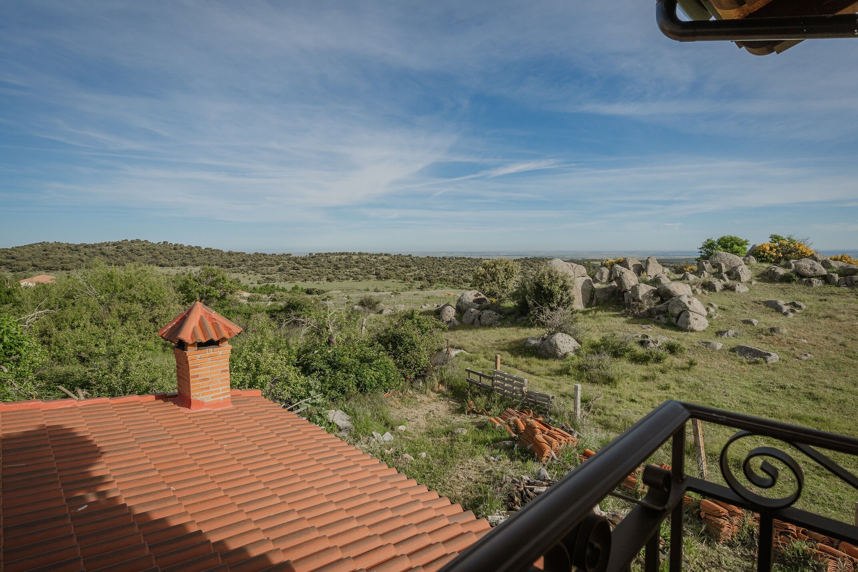 Tejado de tejas rojas, una chimenea de ladrillo y vistas de un paisaje rocoso con vegetación escasa.