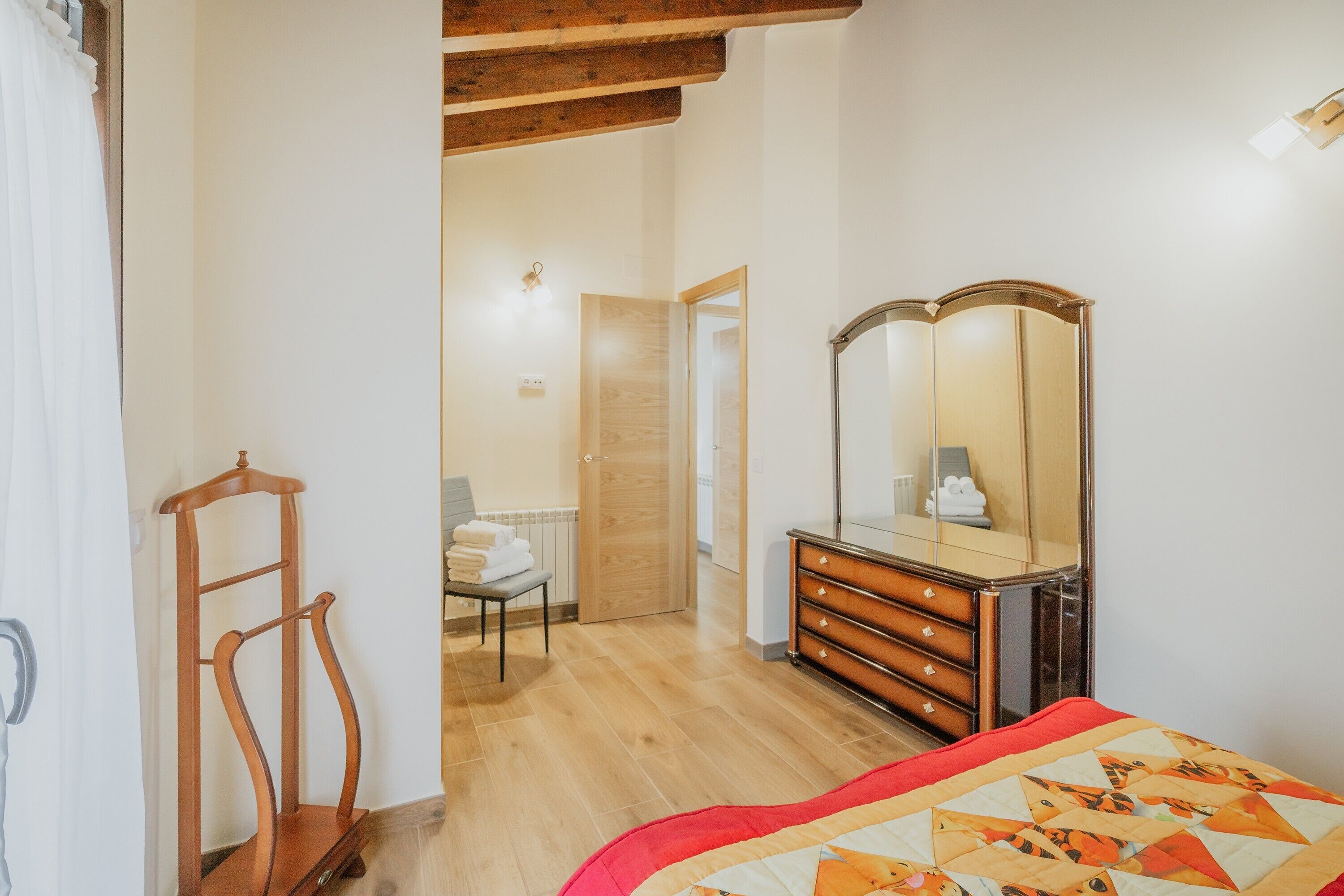 Ein Schlafzimmer mit einem hölzernen Schminktisch, einem Spiegel, einem Bett mit gemustertem Quilten und einem Holzstuhl.