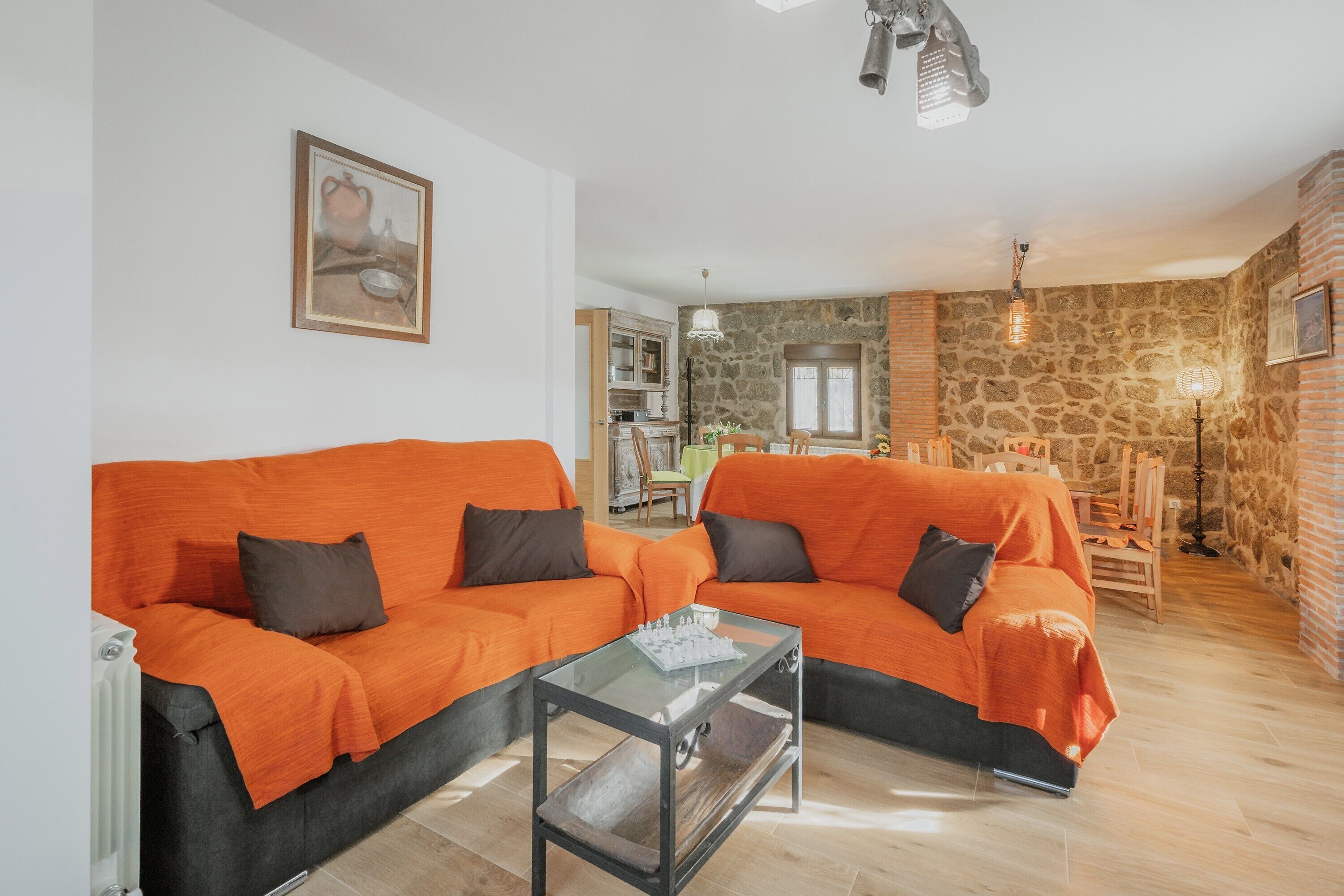 En stue med to orange sofaer, et glasbord, en stenvæg og et køkken i baggrunden.