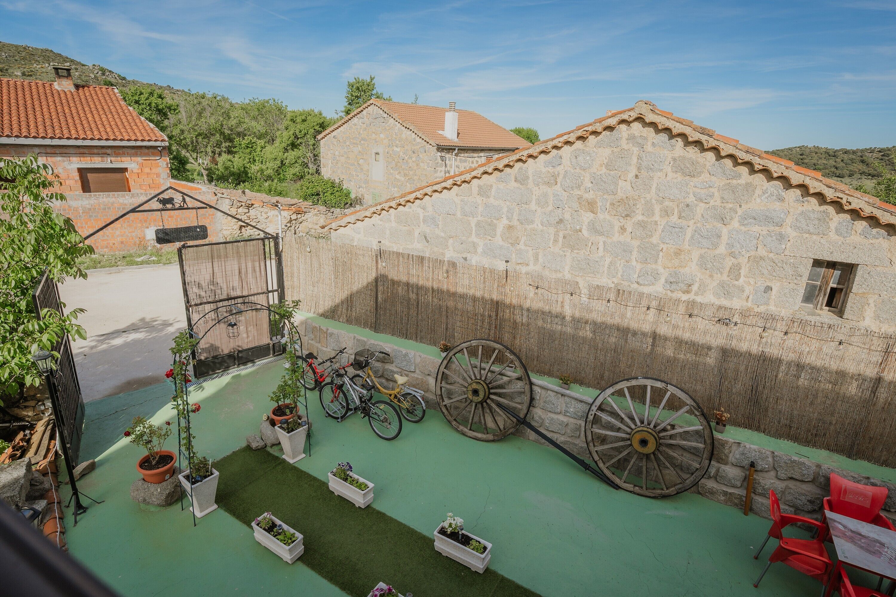 Un patio con muros de piedra, una bicicleta, un carro de madera y plantas en macetas.
