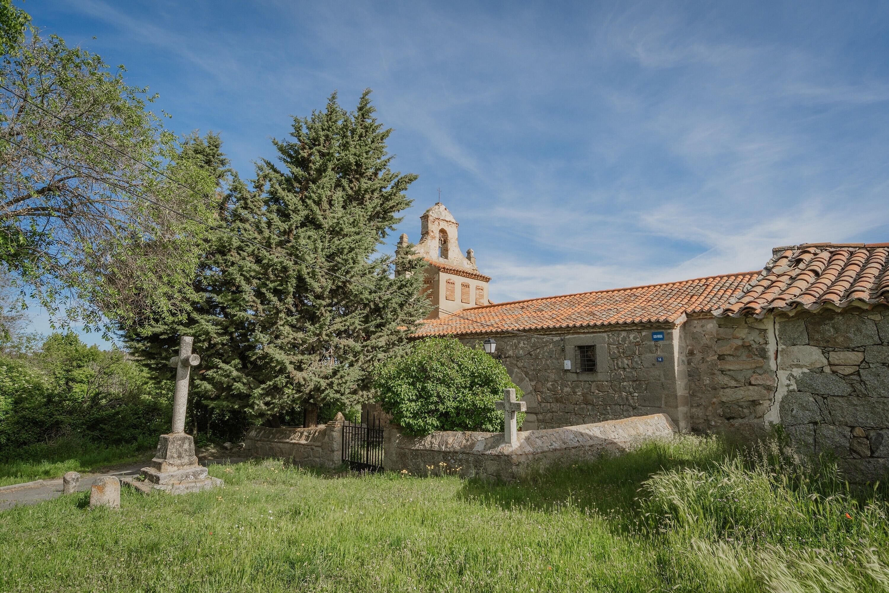 Un bâtiment en pierre, avec un toit en tuiles, une croix et un clocher en arrière-plan.