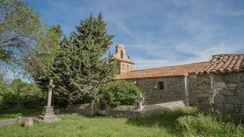 Un bâtiment en pierre, avec un toit en tuiles, une croix et un clocher en arrière-plan.