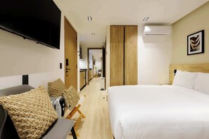 A hotel room with a bed, a TV, a desk with a chair, and a kitchenette in the background. - w* | Amazing Loft w/ Balcony in Parque Mexico (Ciudad de México)