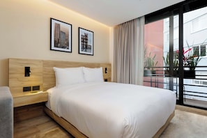 A hotel room with a large bed, a nightstand, a wall-mounted lamp, two framed pictures, and a view through a large window. - w* | Stylish Loft w/ Balcony in Parque Mexico (Ciudad de México)