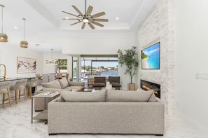 Ein modernes Wohnzimmer mit Sofa, Kamin, Fernseher und Blick auf einen Pool.