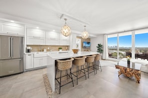 A modern kitchen with a large island, stainless steel appliances, and a city view through large windows. - 1BR+Den Private Residence at Roney Palace (Miami Beach)