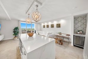 A modern kitchen with a large island, pendant lighting, and a view to the outside. - 1BR+Den Private Residence at Roney Palace (Miami Beach)