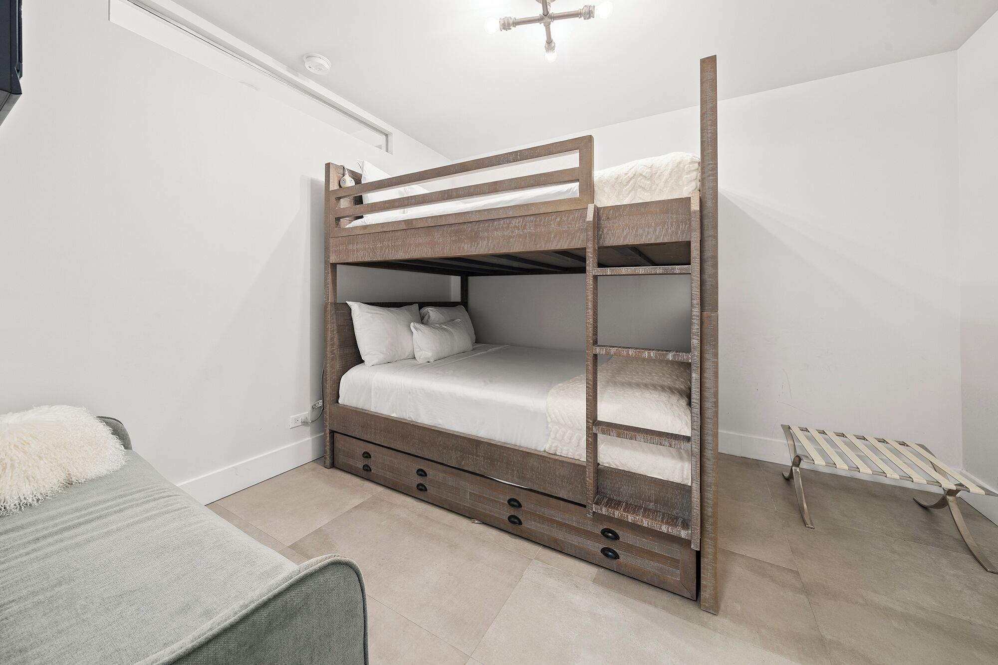 Una cama nido con una escalera, una mesita de noche y un taburete pequeño.