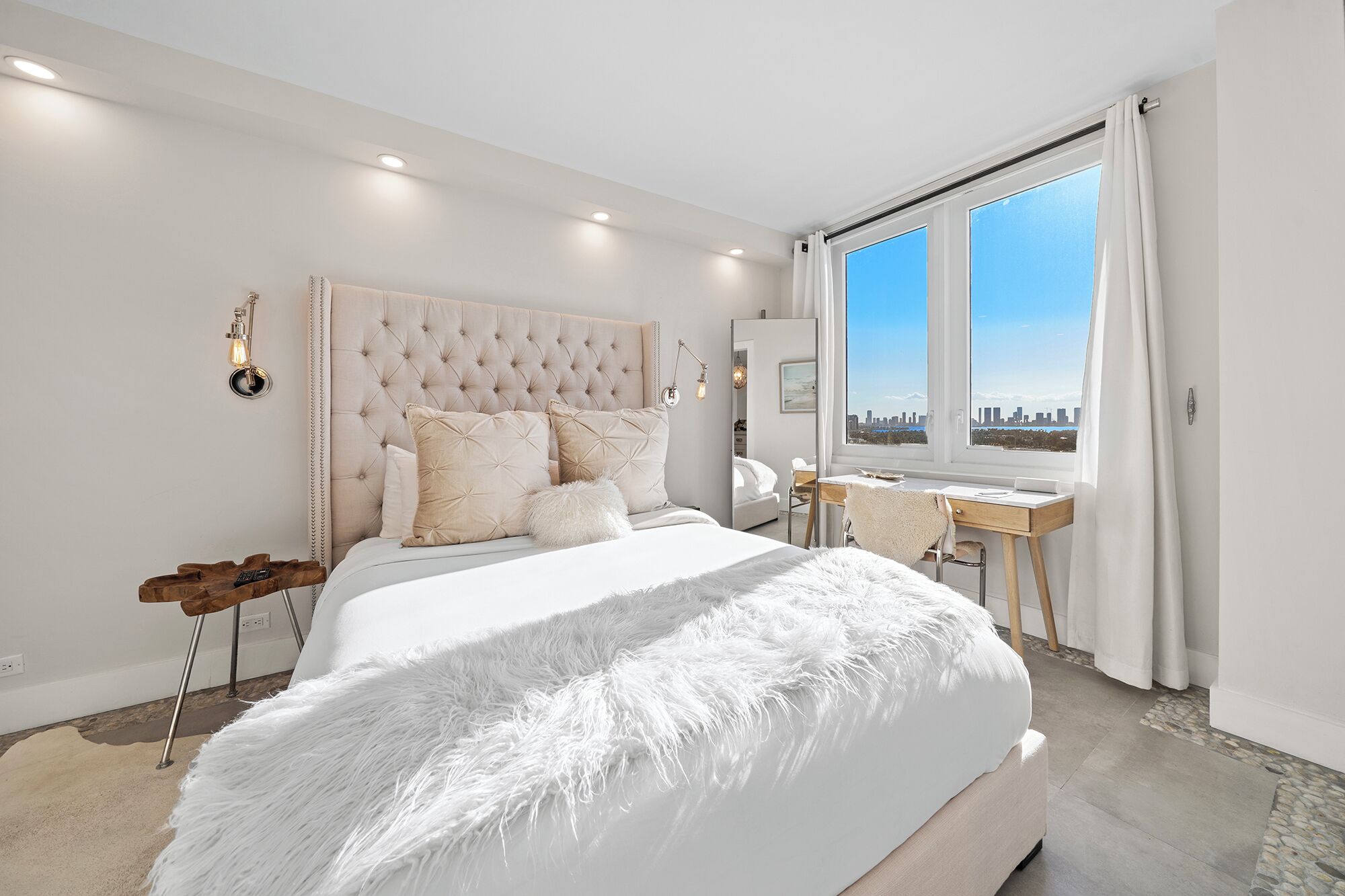 A bedroom with a large bed, a desk, and a view of the city.